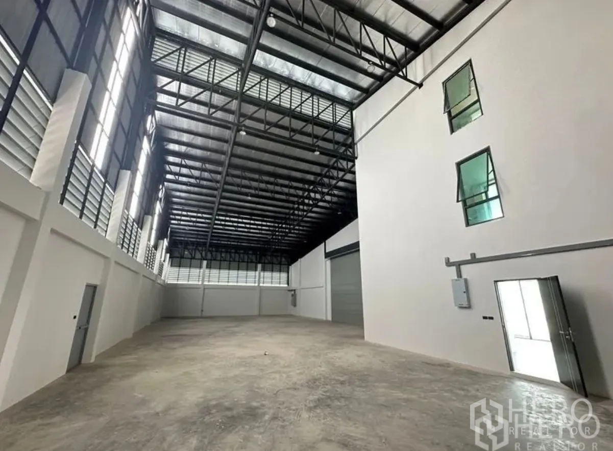 仓库 for sale in Lam Luk Ka, Pathum Thani - 宽阔仓库大厅，侧墙通风百叶、钢屋架与大型卷闸门。