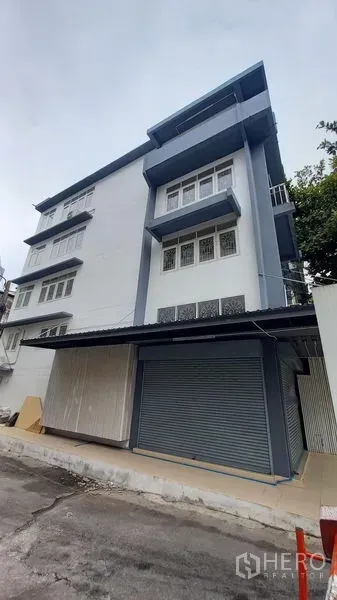 Shophouse for rent in Bangkok - Multi-storey corner shophouse with blue and white facade and metal roller shutter.