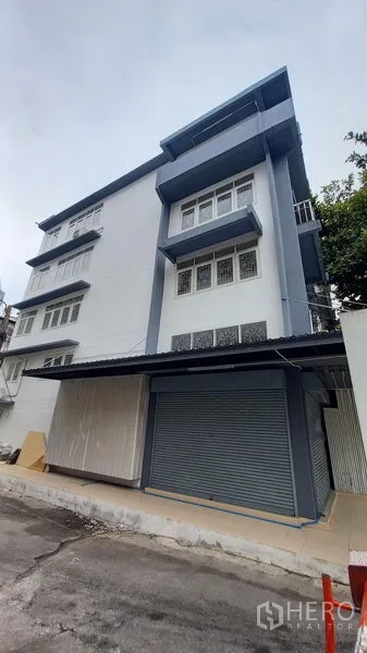 Shophouse for rent in Bangkok - Multi-storey corner shophouse with blue and white facade and metal roller shutter.