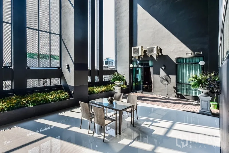 Condominium for rent or sale in Huai Khwang, Bangkok - Private outdoor terrace with dining set, planters, and partial city views.