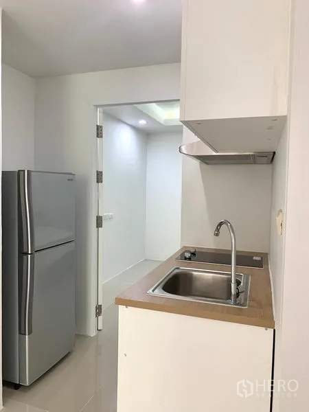 Condominium for rent or sale in Khlong Toei, Bangkok - Compact kitchen with stainless sink, range hood and silver refrigerator along a clean counter.