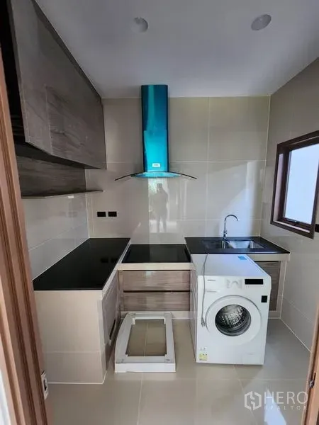 Detached House for rent in Bang Kapi, Bangkok - Compact kitchen with black countertops, cooker hood, sink, window and washing machine.