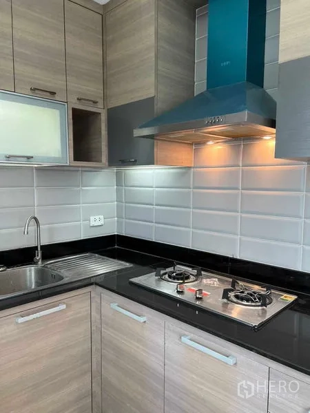 Townhouse for rent in Phra Khanong, Bangkok - Fitted kitchen featuring gas hob, stainless range hood, sink, tiled backsplash and wood cabinetry.