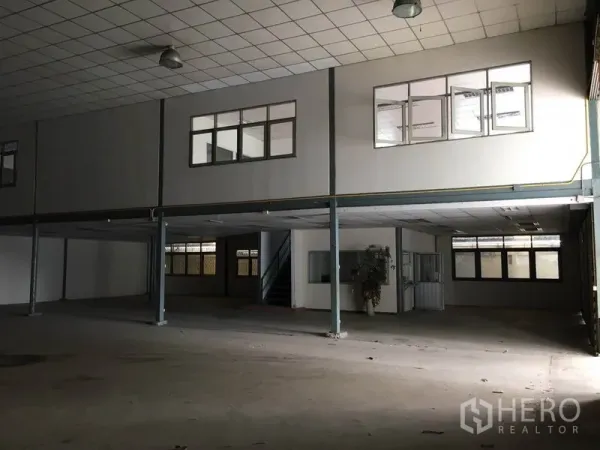 Warehouse for rent in Prawet, Bangkok - Spacious warehouse interior with high ceiling, steel columns, pendant lights and mezzanine offices with windows and stairs.
