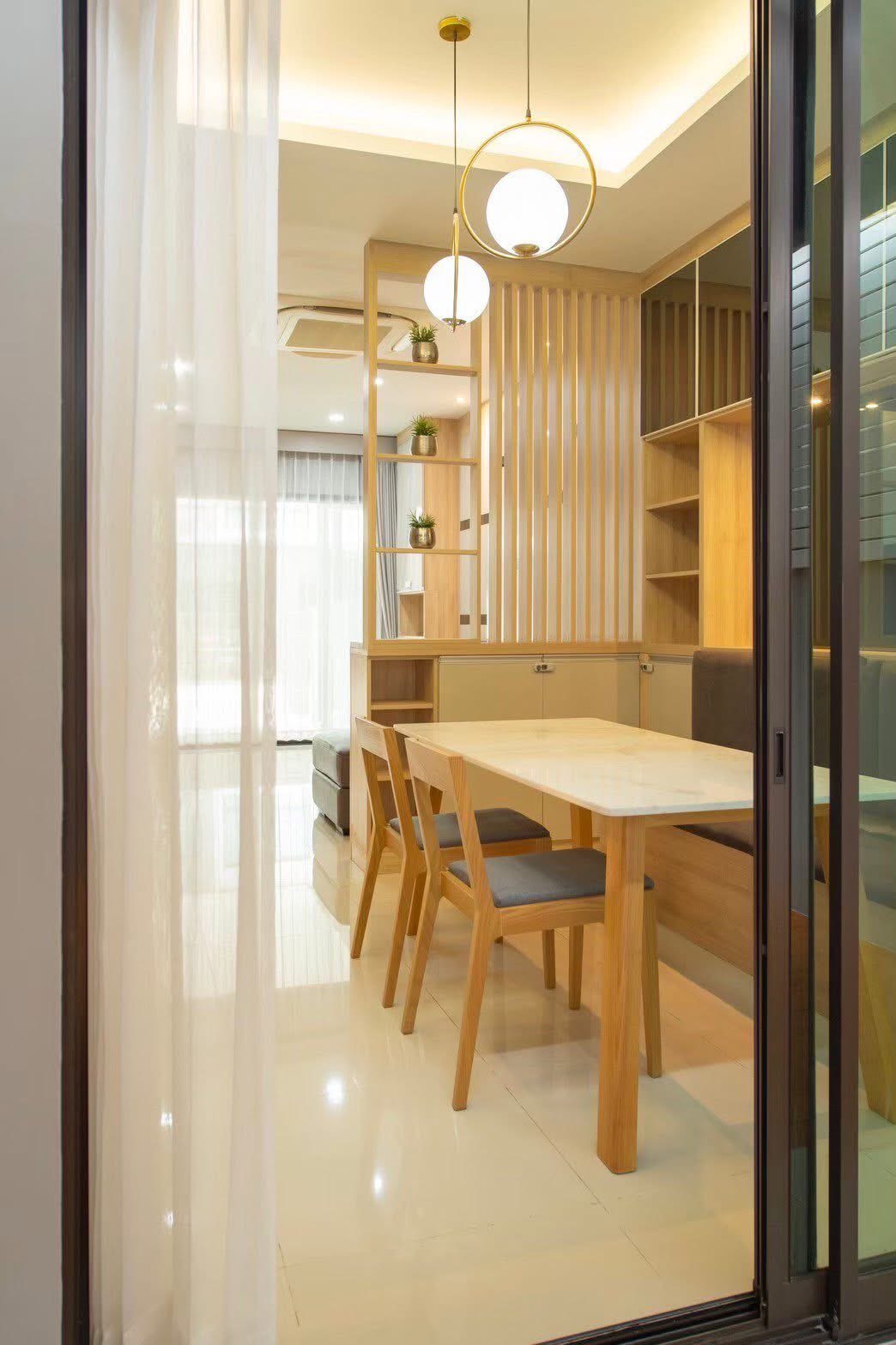 Townhouse for rent or sale in Lat Phrao, Bangkok - View through glass doors to a dining nook with pendant lights and a wooden table.