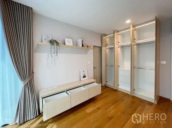 Townhouse for rent or sale in Saphan Sung, Bangkok - Angle view of built-in wardrobes with pull-out drawers beside full-height curtains and wood floors.