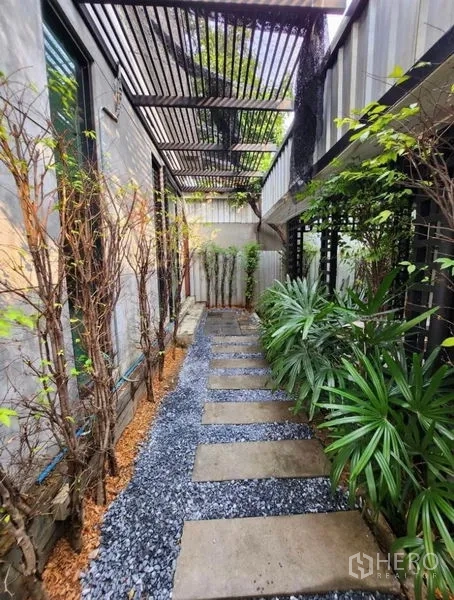 Home Office for rent in Lat Phrao, Bangkok - Shaded side walkway with slatted pergola, gravel and concrete stepping stones lined with tropical plants.
