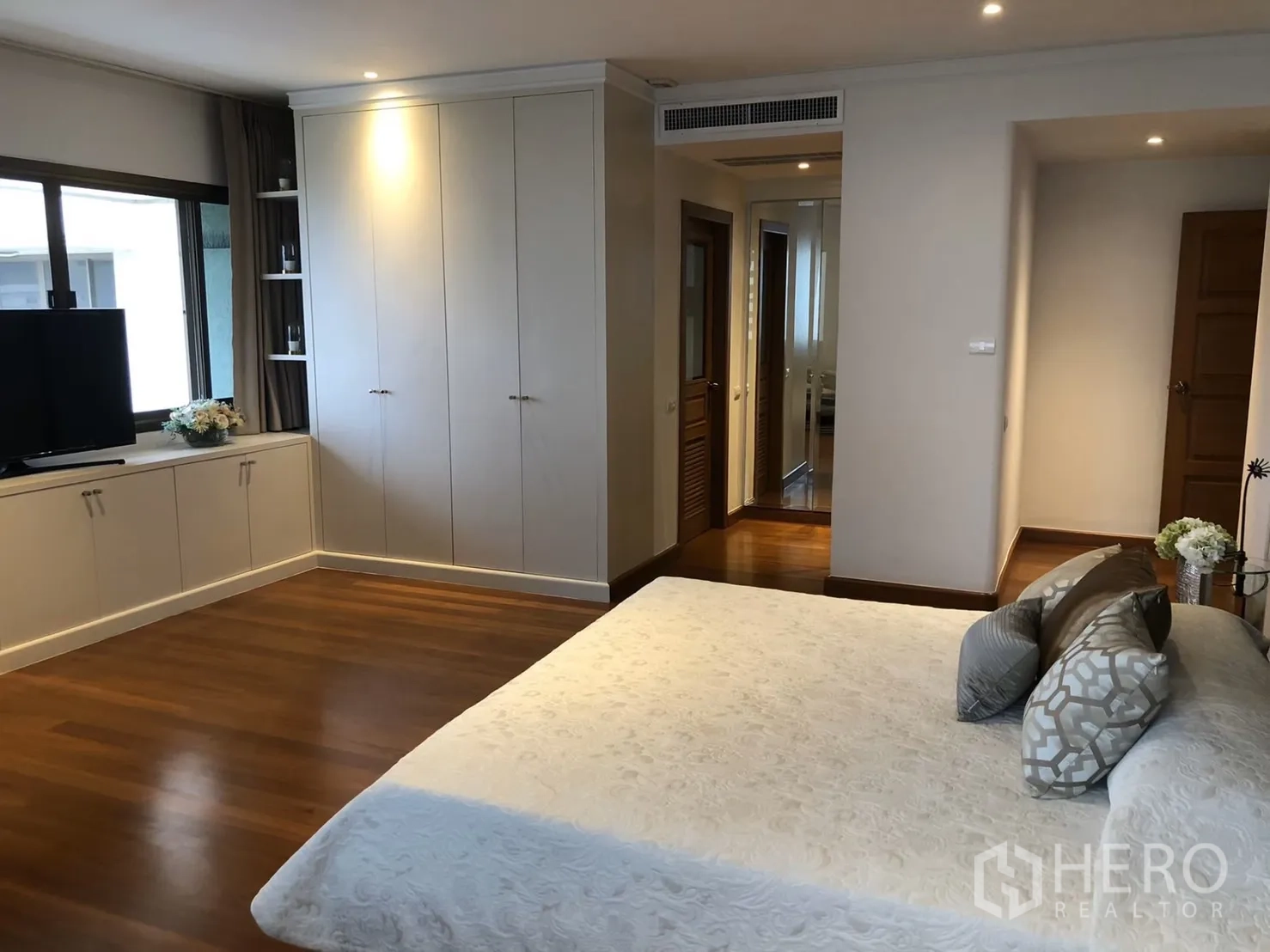 Condominium for rent in Bangkok - Corner of bedroom with built-in cabinets, TV and warm wood flooring.