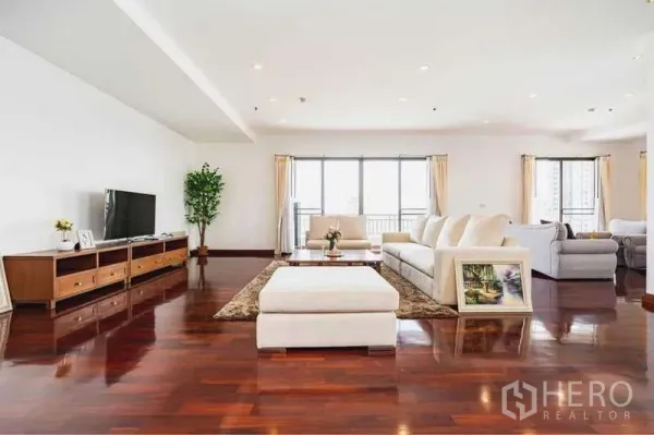 Apartment for rent in Sathon, Bangkok - Expansive living room with white sofas, TV console, polished wooden floors and multiple windows to the balcony.
