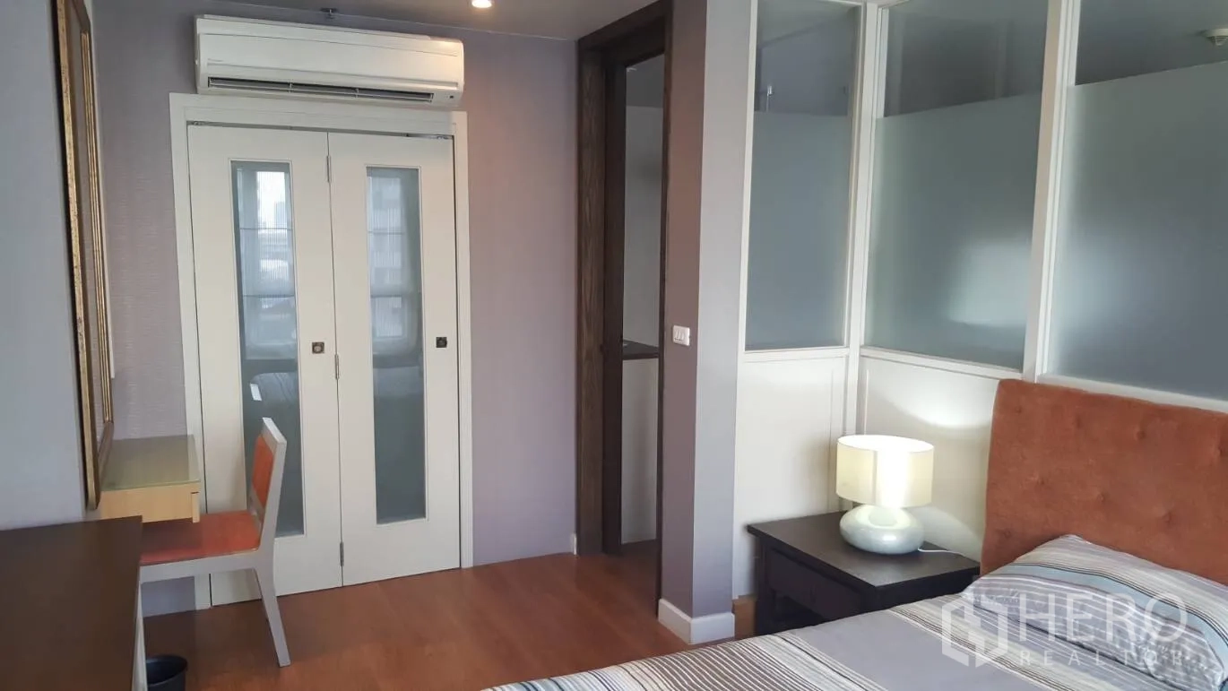 Condominium for rent in Khlong Toei, Bangkok - Bedroom view with sliding glass doors, study nook and air conditioner above.