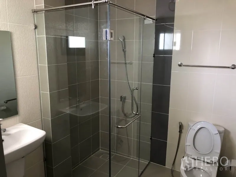 Detached House for rent in Prawet, Bangkok - Bathroom with glass-enclosed corner shower, toilet and compact basin.