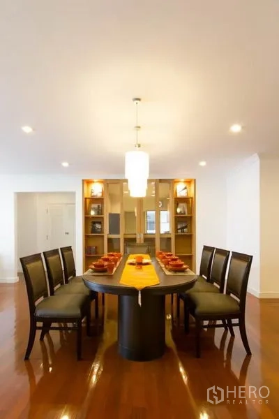 Condominium for rent in Watthana, Bangkok - Formal dining room with an oval table, eight chairs, pendant light and built‑in display shelves.
