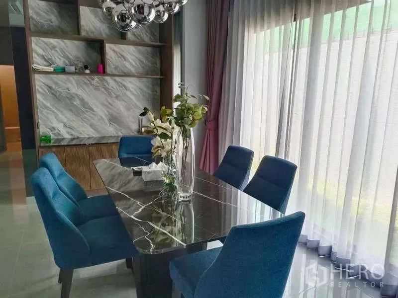 Detached House for rent in Bang Phli, Samut Prakan - Modern dining area with black marble table, blue upholstered chairs and full-height sliding glass doors.