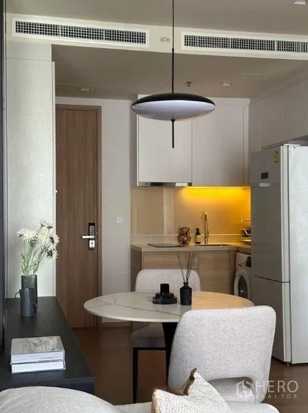 公寓 出租在Watthana, Bangkok - 紧凑厨房：白色柜体、暖色背光、冰箱与洗衣机，旁有圆桌。
