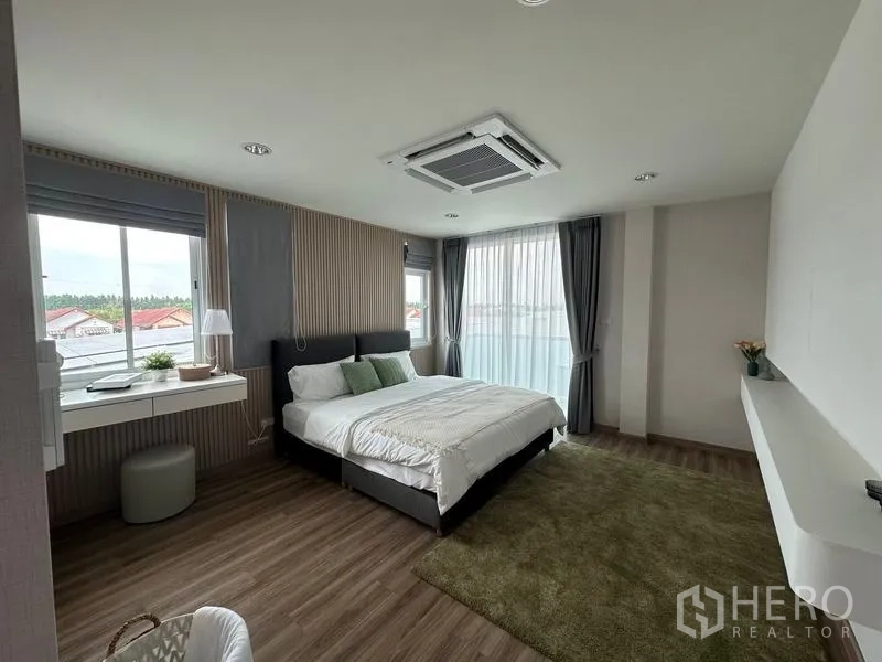 Warehouse for sale in Pathum Thani - Spacious master bedroom with large windows, green rug and ceiling cassette air-conditioner.