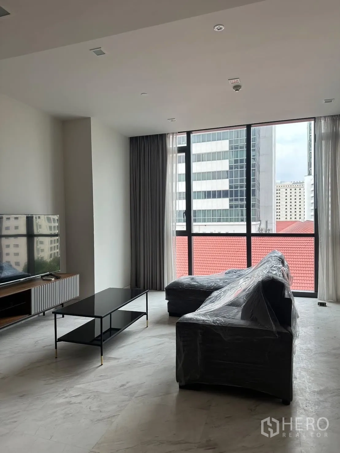 คอนโด for rent or sale in Watthana, Bangkok - ห้องนั่งเล่นสว่างพร้อมโซฟาเข้ามุม ชั้นวางทีวี และหน้าต่างสูงจรดเพดาน.