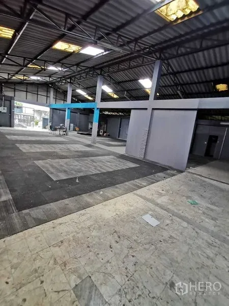 Warehouse for rent in Nonthaburi - Open‑plan warehouse interior with steel truss roof, skylights and gray partition rooms.
