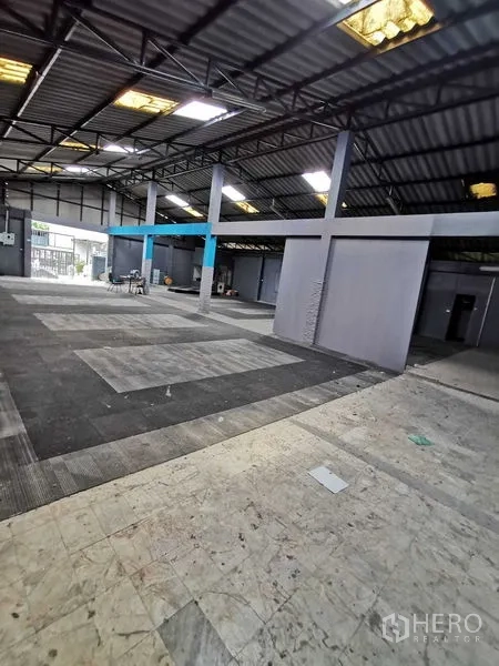 Warehouse for rent in Nonthaburi - Open‑plan warehouse interior with steel truss roof, skylights and gray partition rooms.