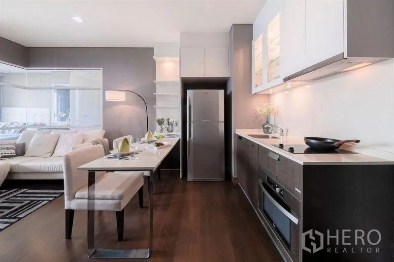 Condominium for rent or sale in Watthana, Bangkok - Compact kitchen with built-in appliances and dining table beside the lounge.