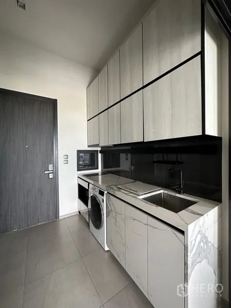 Condominium for rent in Phra Khanong, Bangkok - Entry galley kitchen with ample overhead storage, stone countertops, sink and appliances.