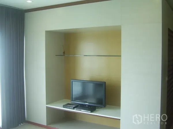 Condominium for rent in Khlong Toei, Bangkok - Built-in TV wall with glass shelf and grey blackout curtains in a modern condo living area.