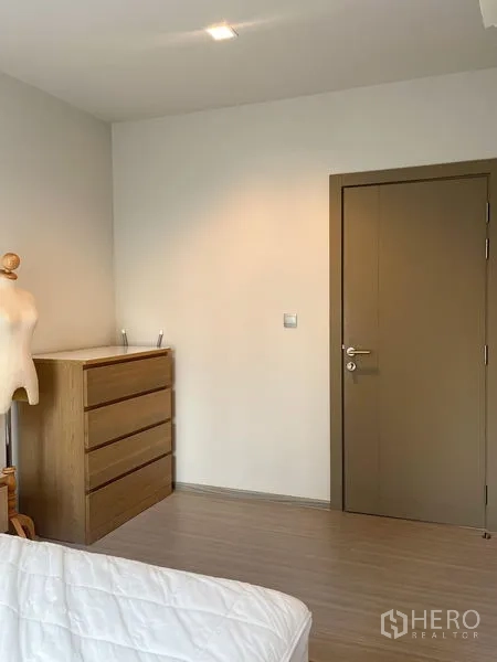 公寓 出售在Ratchathewi, Bangkok - 卧室一角，木质抽屉柜、素色墙面与关闭的室内门。
