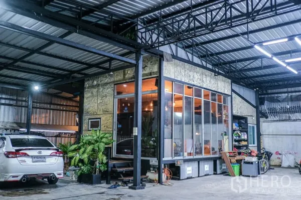 Warehouse for rent in Bueng Kum, Bangkok - Steel-frame warehouse in Bueng Kum with a glass-front office pod and covered parking at night.