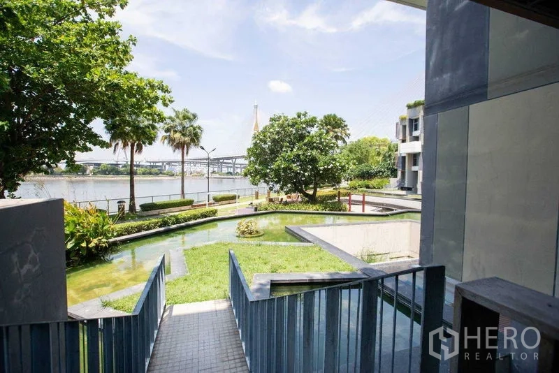 Condominium for rent in Yan Nawa, Bangkok - Landscaped riverside garden with pond and distant bridge view.