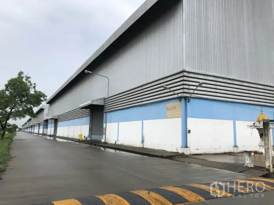Warehouse for rent in Phra Nakhon Si Ayutthaya - Side view of warehouse facade with multiple roller doors and street lighting along a concrete road.