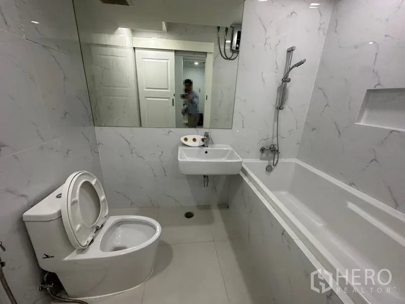 Condominium for rent in Watthana, Bangkok - Bathroom with bathtub, handheld shower, wall mirror and white tiles.