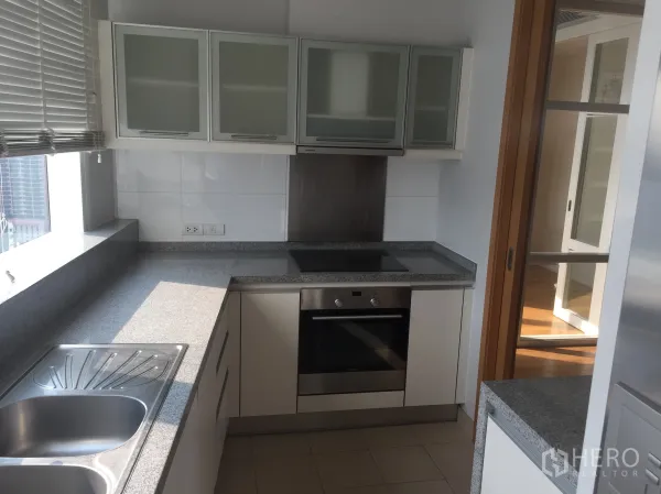 Condominium for rent in Khlong Toei, Bangkok - Modern closed kitchen with granite countertops, built-in oven, and a large window.