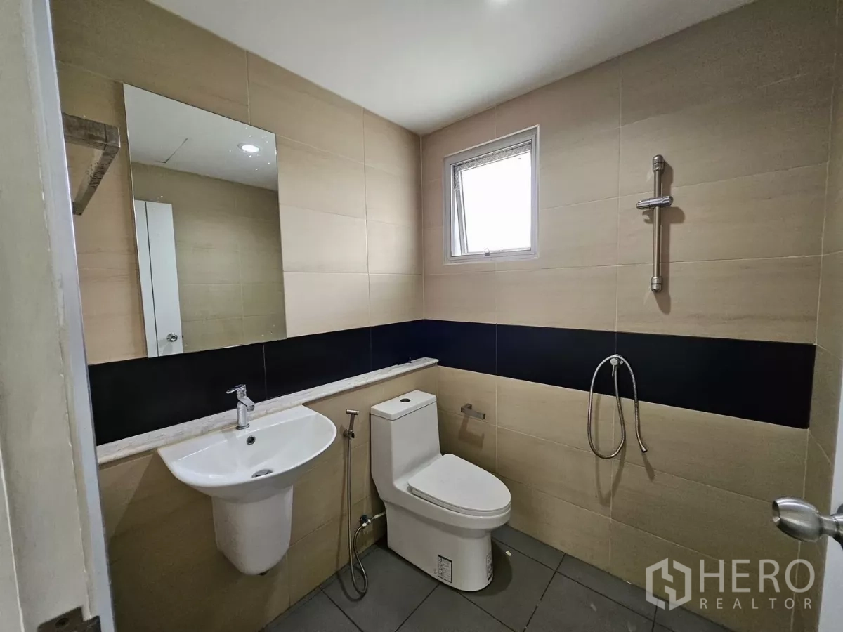Detached House for rent in Khlong Toei, Bangkok - Bathroom with beige tiles, window, toilet, handheld bidet spray and shower fittings.