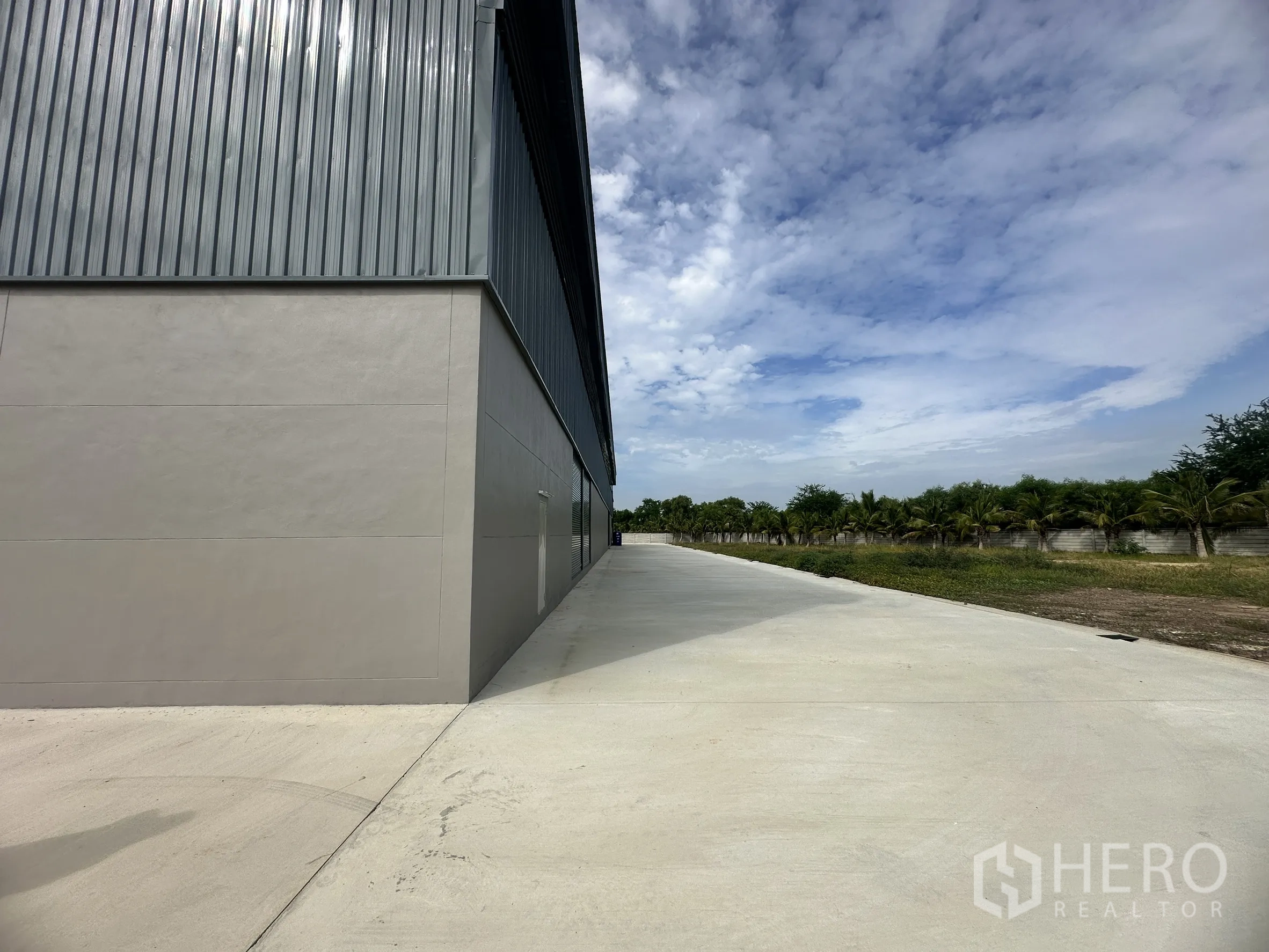 工厂 for rent or sale in Bang Len, Nakhon Pathom - 仓库侧边的长混凝土通道，边界种有树木。