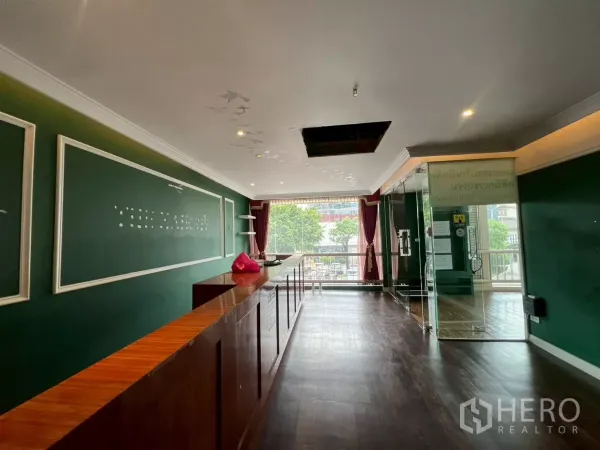 办公空间 出租在Watthana, Bangkok - 接待区配深色木地板与绿色特色墙，前方大窗与玻璃门，适合办公室或零售。